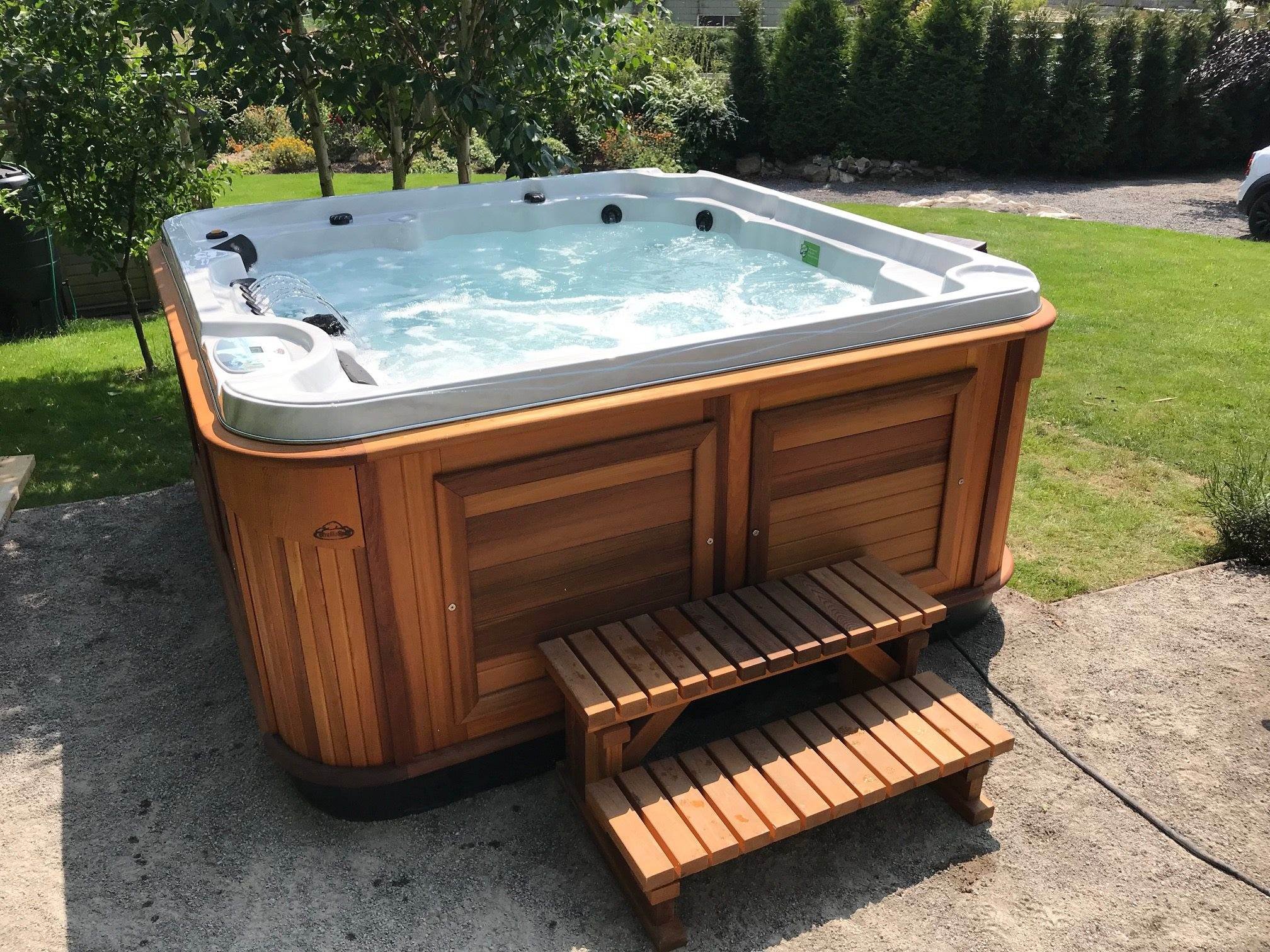 Wood-paneled hot tub with bubbling water and small wooden steps on a concrete surface in a garden.