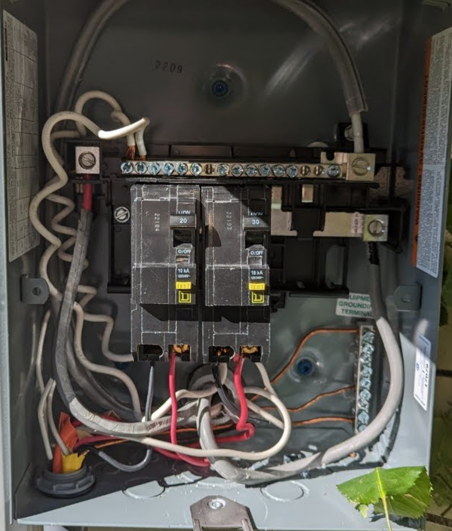 Open electrical breaker panel with two circuit breakers labeled 20 and 30 amps, multiple connected wires, and grounding terminals.
