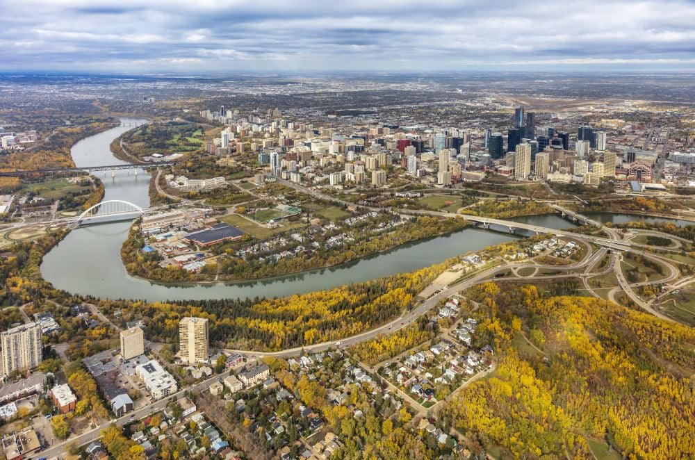 Aerial view of a city skyline with a river curving through residential and park areas.