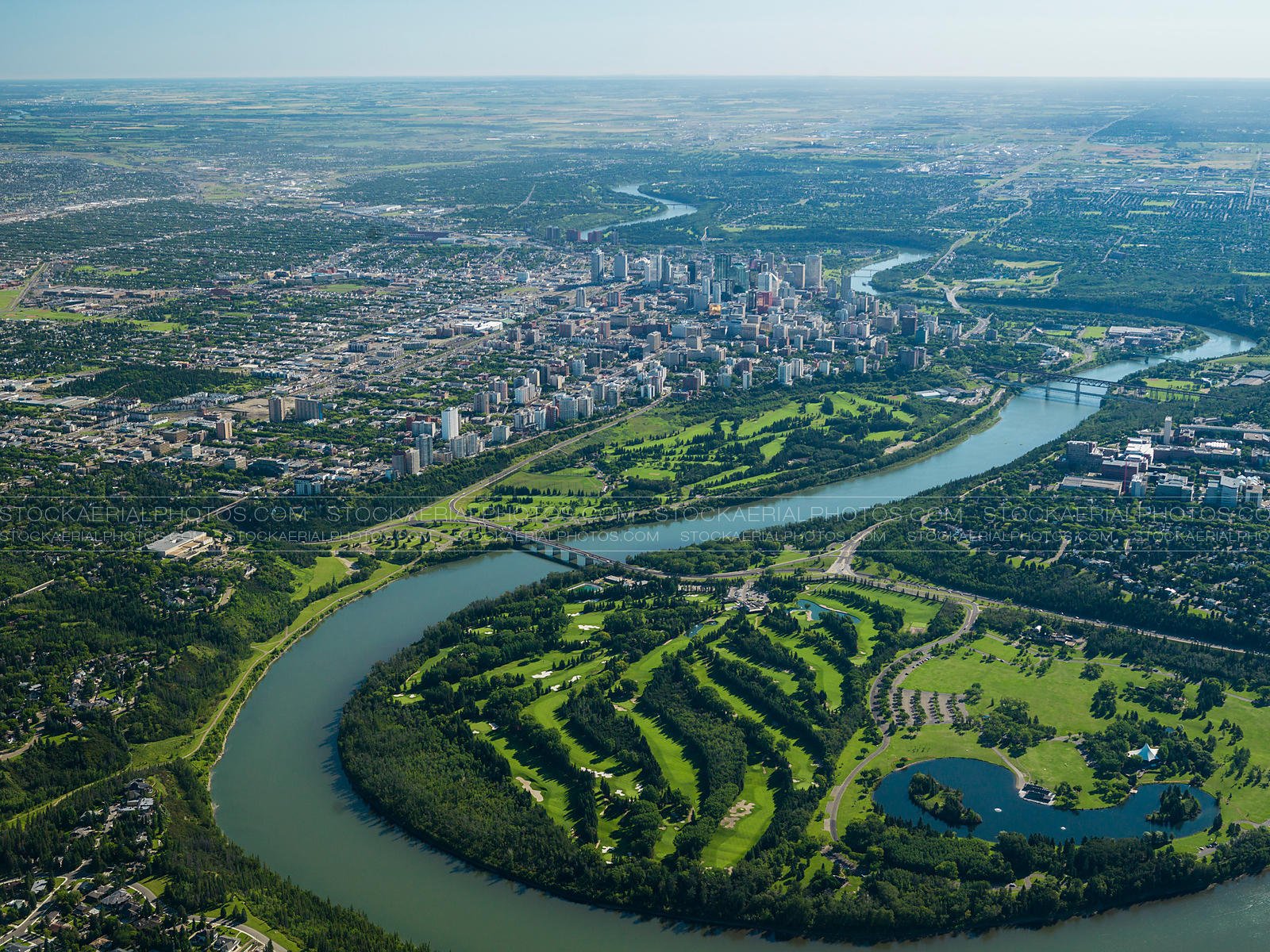 Aerial view of a city with a river curving around a large green golf course and parkland.