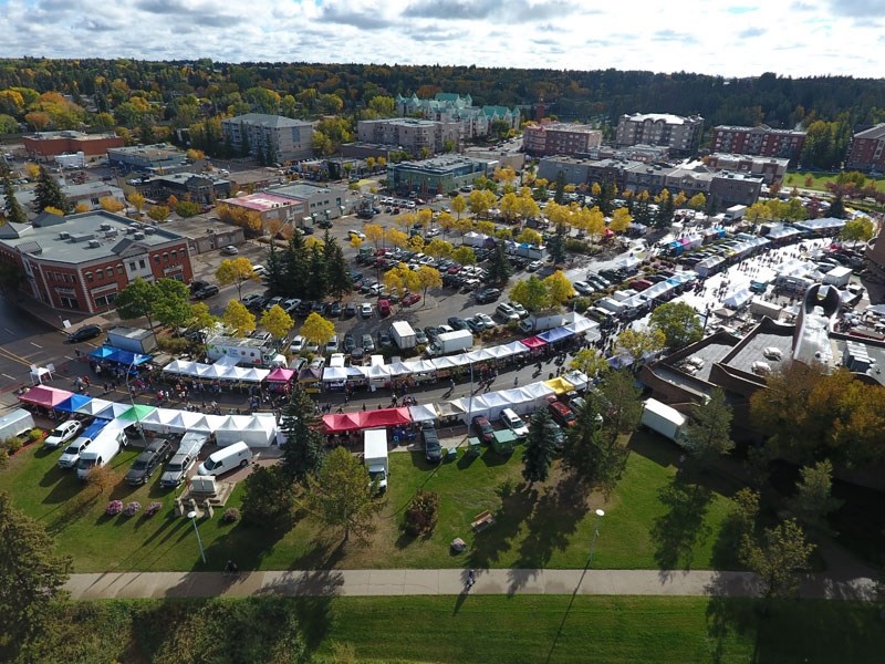 Aerial view of a town market with colorful tents and surrounding buildings and trees in autumn.