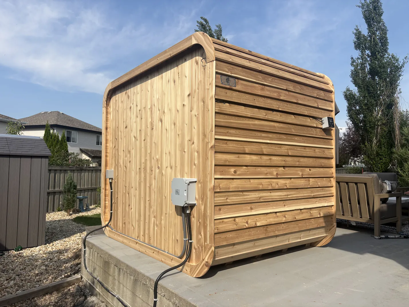 Wood-paneled hot tub with bubbling water and small wooden steps on a concrete surface in a garden.