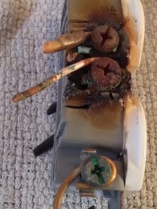 Close-up of a severely burnt electrical outlet with melted and charred screws and wires.