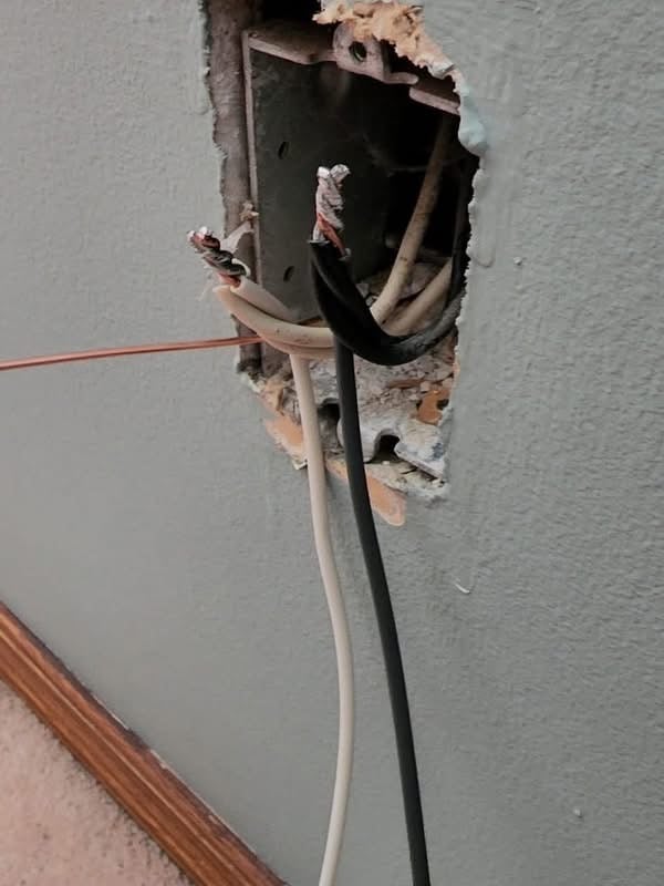 Exposed electrical wiring with stripped ends protruding from an electrical box in a gray wall.
